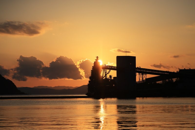 火力発電所の岸壁に並ぶ、アンローダ（石炭を降ろす装置）に夕日が沈んでいきます。