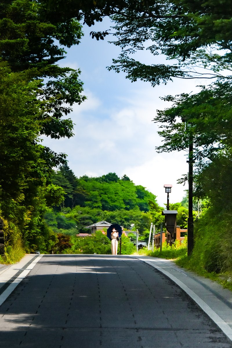 軽井沢の追分宿，旧国道の緩やかな坂道を越したあとに振り返ると，夏の青空のもとで日傘さしながら自撮りするご婦人の姿．モネ「日傘をさす女」を意識して．