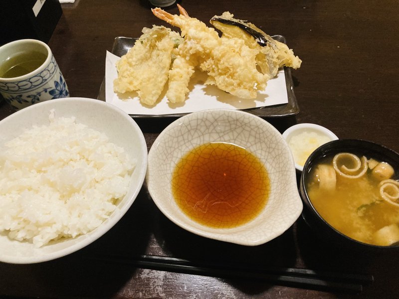 今日は、地元神保町の【天ぷらはちまき】さんで遅めのお昼。天ぷら定食1000円。海老2本、イカ、キス、レンコン、ナス、カボチャ、ピーマンの盛り合わせ。テーブルには、秘伝の天丼たれ、新生姜とごぼうのガリのようなおしんこ、塩、七味、緑茶がセットされています。しかもご飯おかわり自由。このともすればどこにでもありそうなシンプルな天ぷら定食、ところがドッコイ。サクッと薄衣で揚げられた上質の天ぷらに丁寧な仕事が見えます。キリッと醤油の効いた天丼たれ。おしんこも手作りなのかな、いい箸休め。夢中で食べた、至福のひととき。