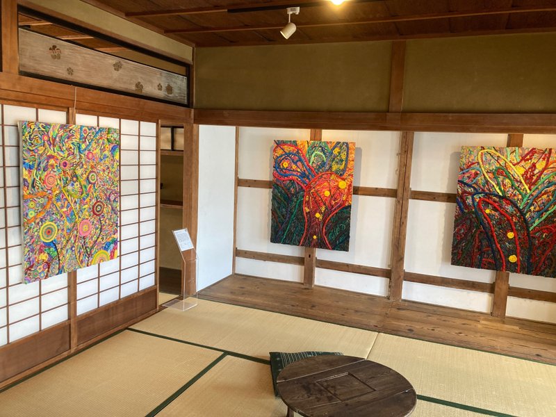 2階の和室に展示されている3枚のキャンパス作品。赤色や青色、水色、黄色、緑色といった色のあるカラフルな作品。花のようなうずまき模様や葉っぱの形が見える。