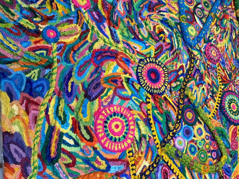 作品の拡大画像。キャンパス地の色とその上に貼られた紐や毛糸が組み合わさって、花のような、渦のような、ペイズリーガラのような不思議な模様になっている。