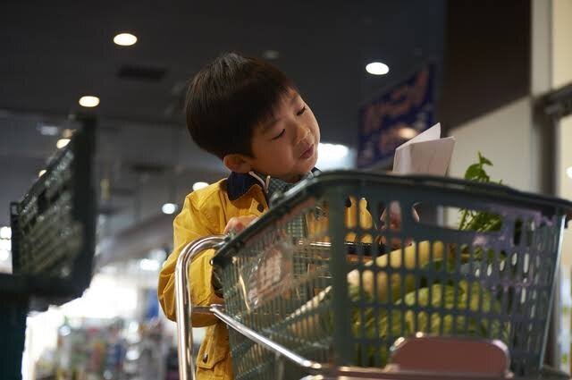 スーパーでカートを押しながらメモを読んでいる男の子の写真