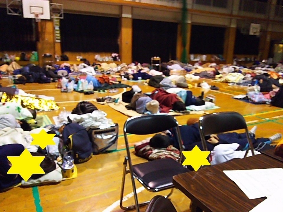 体育館で避難者が毛布で寝ている画像　照明がすべて点いていて明るい中で皆が寝ている