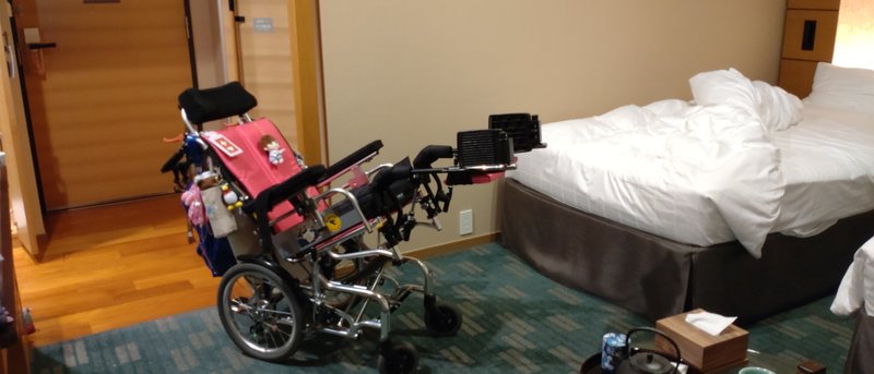 右にベッド、真ん中にヘッド付き介助式車椅子、左にドア