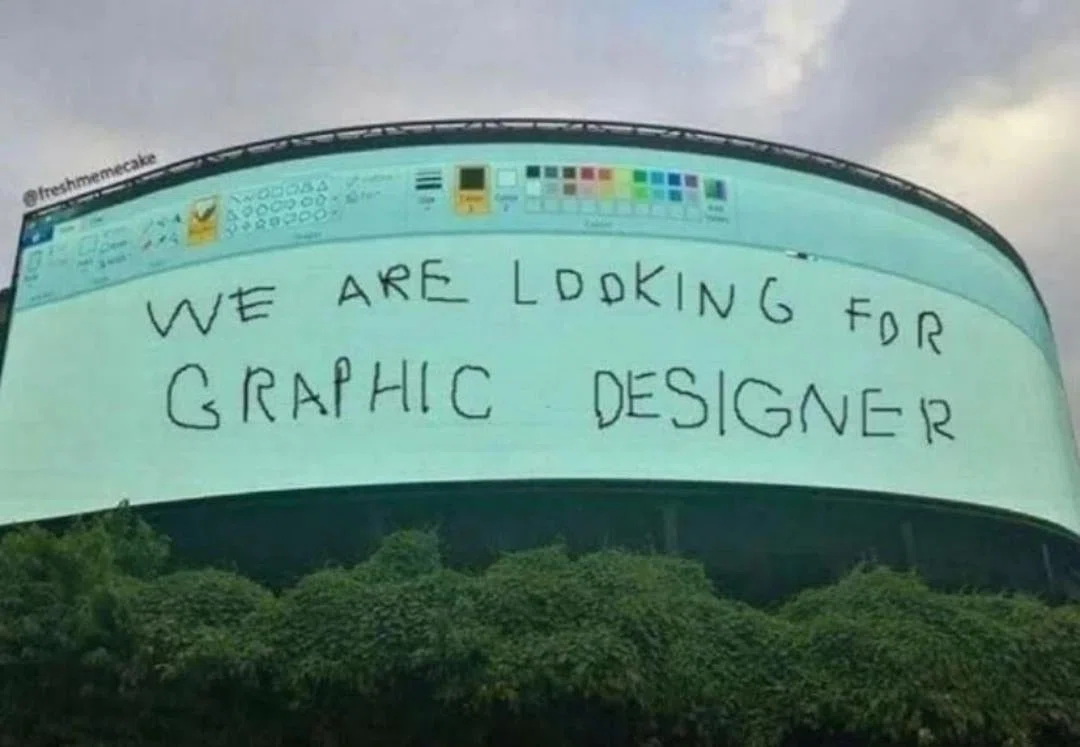 ビル壁面の大型ディスプレイにWindowsのペイントソフトの画面。ペイント上には拙い字で「WE ARE LOOKING FOR GRAPHIC DESIGNER」と書かれている。