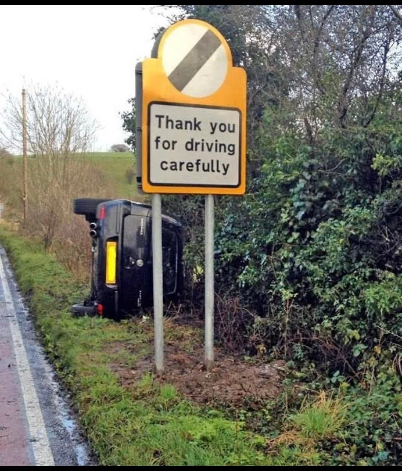 Thank you for driving carefullyと書かれた道路脇の看板の後ろで、横転している車