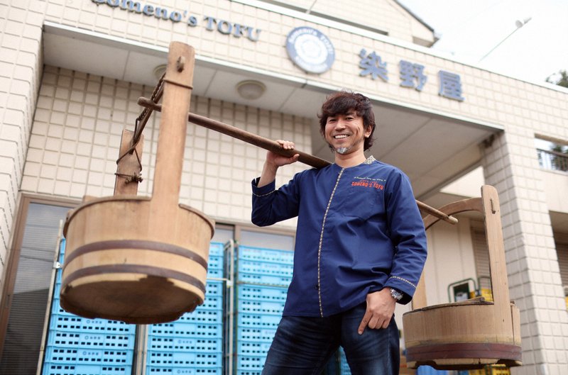 かつて豆腐の販売で使われていたおけを肩に乗せ、ポーズをとる染野屋の小野篤人社長=小川昌宏撮影