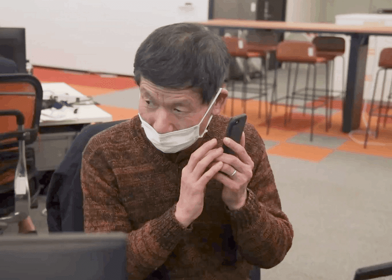 アクセシビリティアナリストの和田が、スマートフォンの音声読み上げ機能を使っている様子。耳に端末を近づけ、読み上げ音声を聞いている。