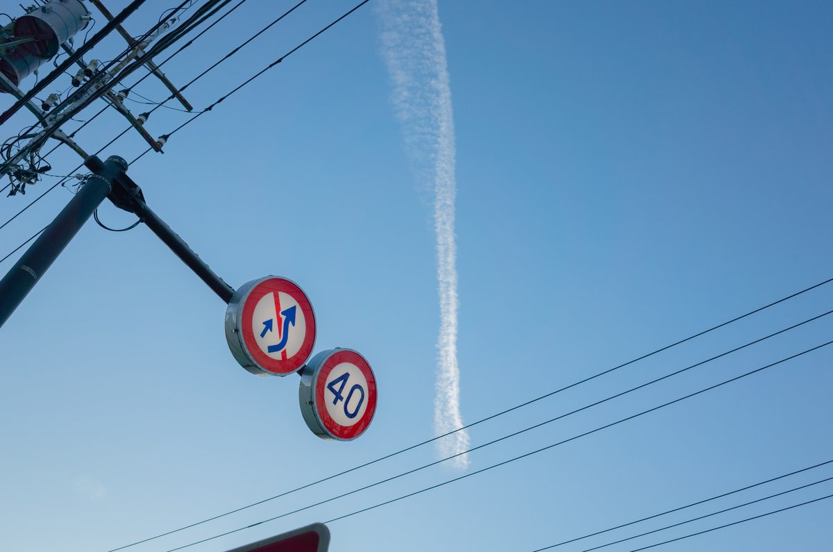 空を見上げた写真。飛行機雲とその手前に標識が写っている。