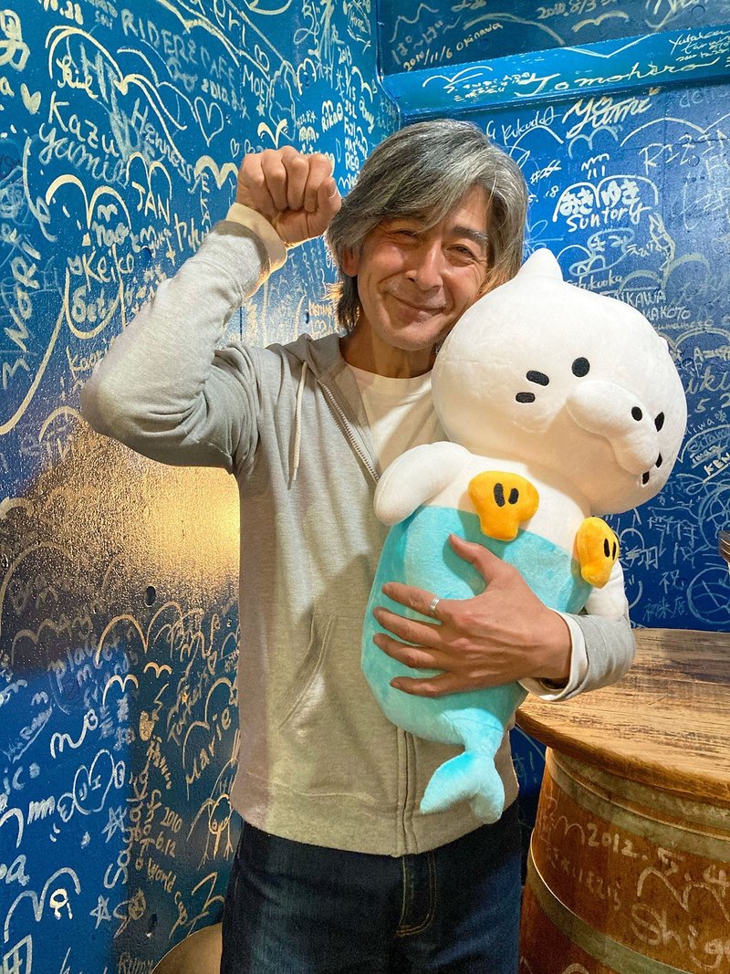 高尾さんが猫のポーズをしておっとにゃんぬいぐるみを抱いている画像