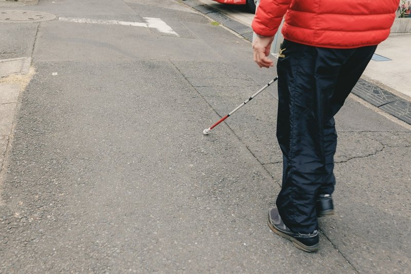 路上を白杖を使って歩く重田さんの写真