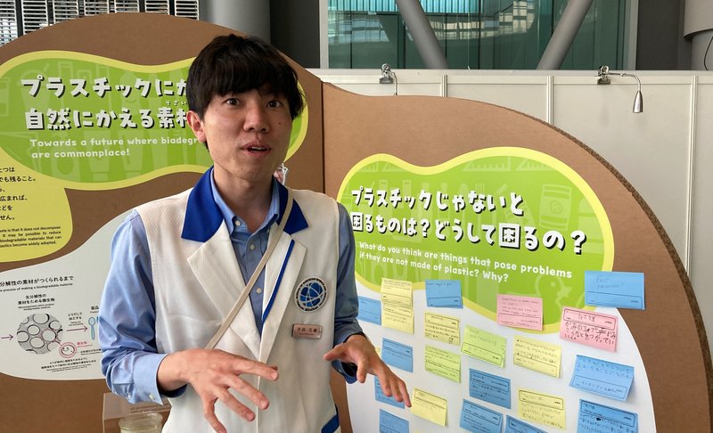 Green Planet の展示を背景に話してくれている科学コミュニケーターの平井さんの画像