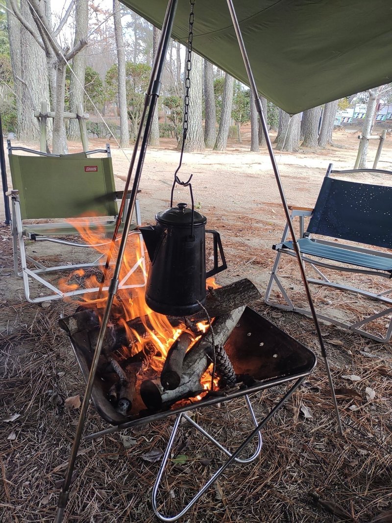 屋外で、焚火の横にキャンプ用の椅子が２脚おいてある写真。