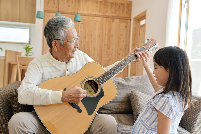 高齢者がギターを孫に教えている画像