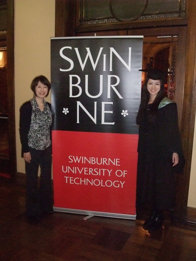 SWINBURNE UNIVERSITY OF TECHNOLOGYと書かれたプルアップバナーとともに映るガウンを着た花恵さん