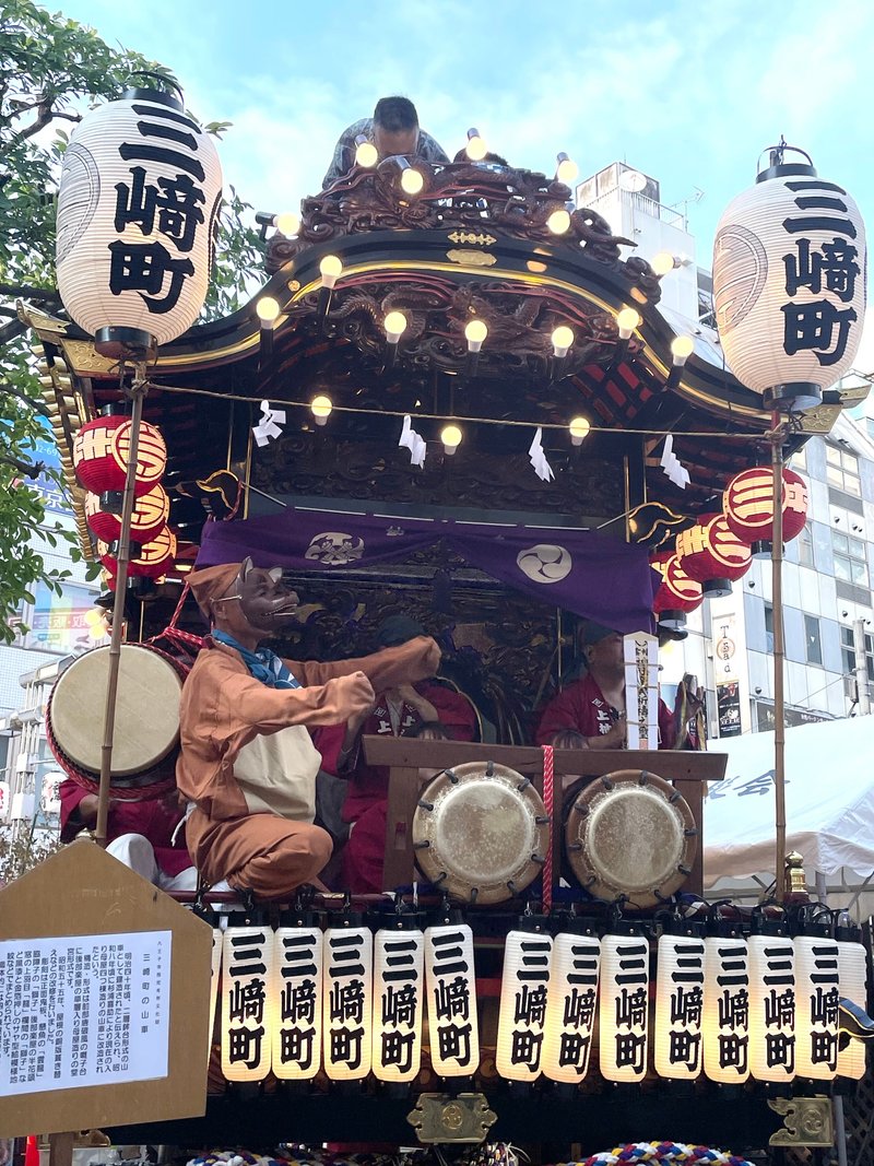 写真・山車の上でたぬきと思しき面をかぶって踊っている人