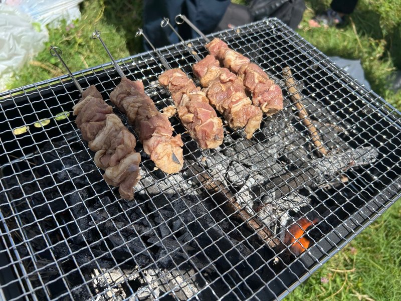 BBQコンロの網の上で、鉄串に刺された羊肉が焼かれている写真。