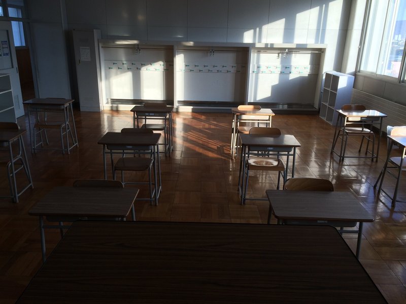 12 セットの机と椅子が並んだ教室を教卓から眺めた景色の写真