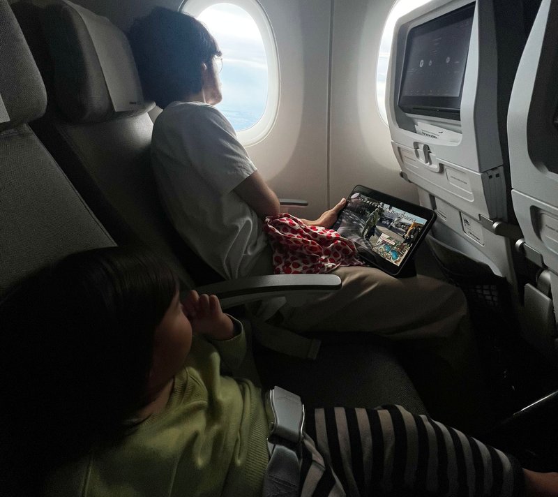フィンエアーの機内の座席でくつろぐ、藤間の娘と藤間の夫。夫は窓の外を眺めながら、娘にタブレットで動画を見せている