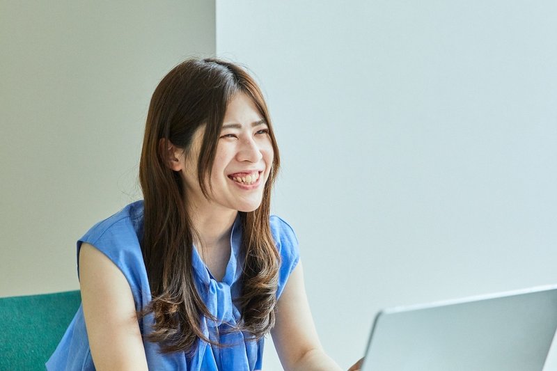 右手を向いてパソコンを前に座り、笑っている女性の写真。