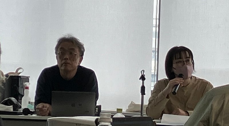 写真登壇者として岡本先生と渡邉さんが、並んで着席しています。手にマイクを持った渡邉さんがあはきの仕事の魅力を伝えるプロモーションビデオについて説明しています。