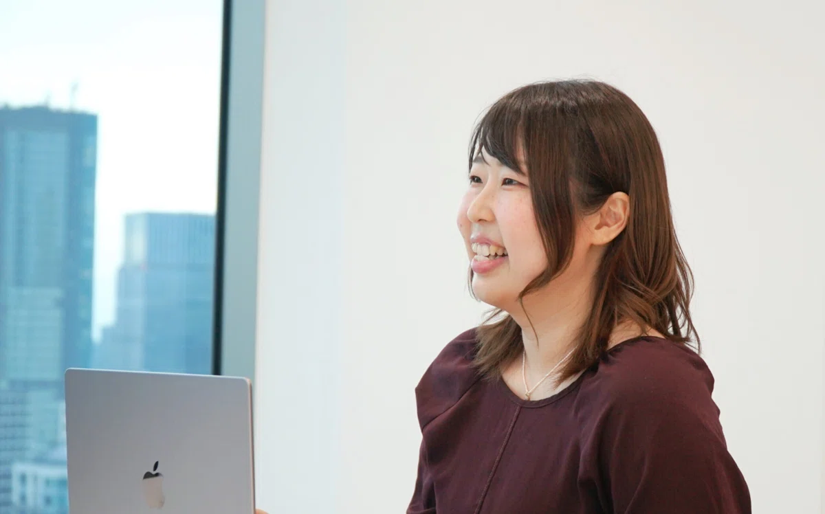パソコンを前に座り、左側を向いて微笑む女性の写真。