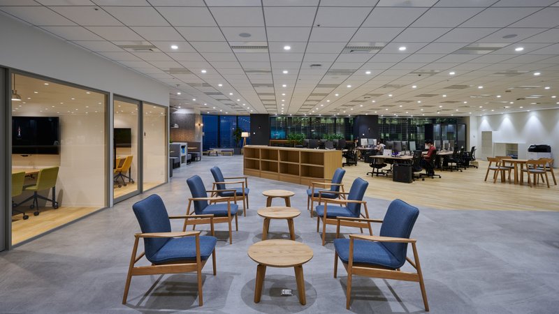 青色の椅子が2脚ずつ向き合って3セット置かれており、左手には会議室が、右奥には執務室が見える写真。