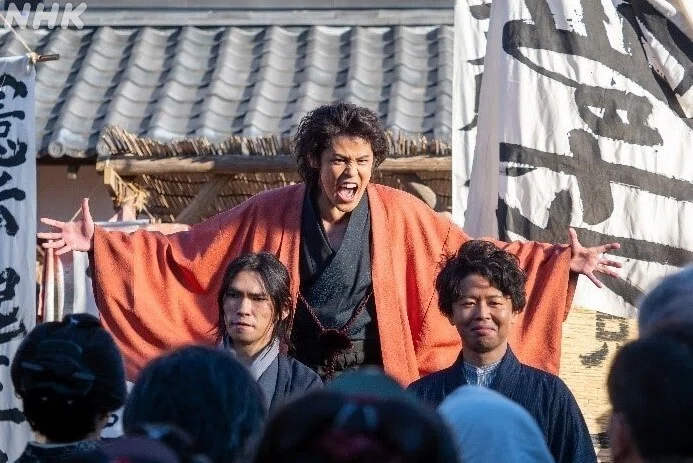 劇中写真:オレンジ色の羽織を着て演説する早川逸馬(演・宮野真守さん)