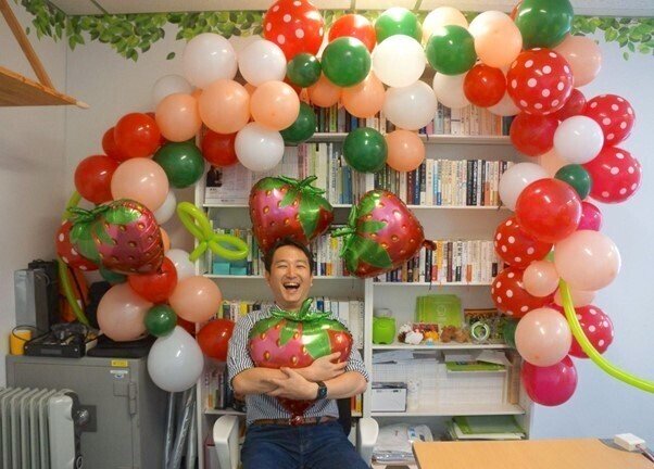 たくさんのバルーンといちご型のバルーンで飾られた社長室でにこやかに笑う森社長の写真