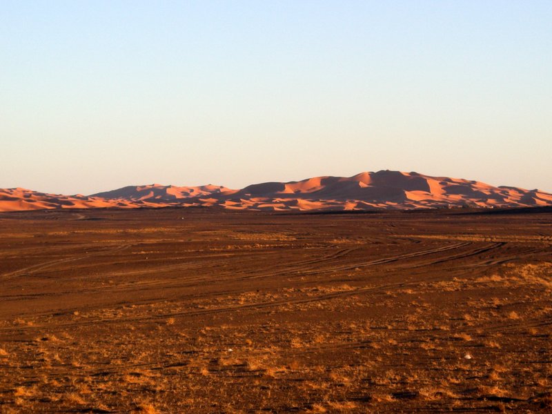 赤い荒野の向こうにサハラ砂漠の砂丘群が見える