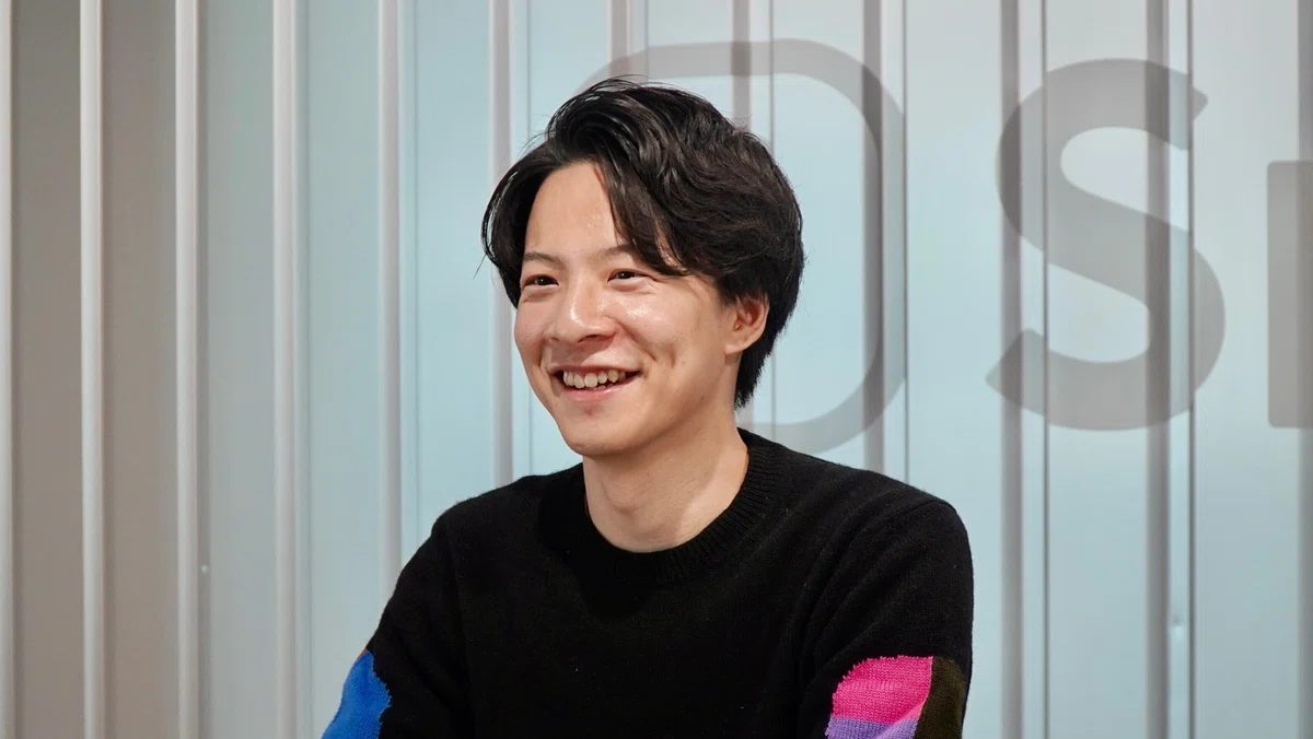 左側を向いて微笑みながら話す男性。
