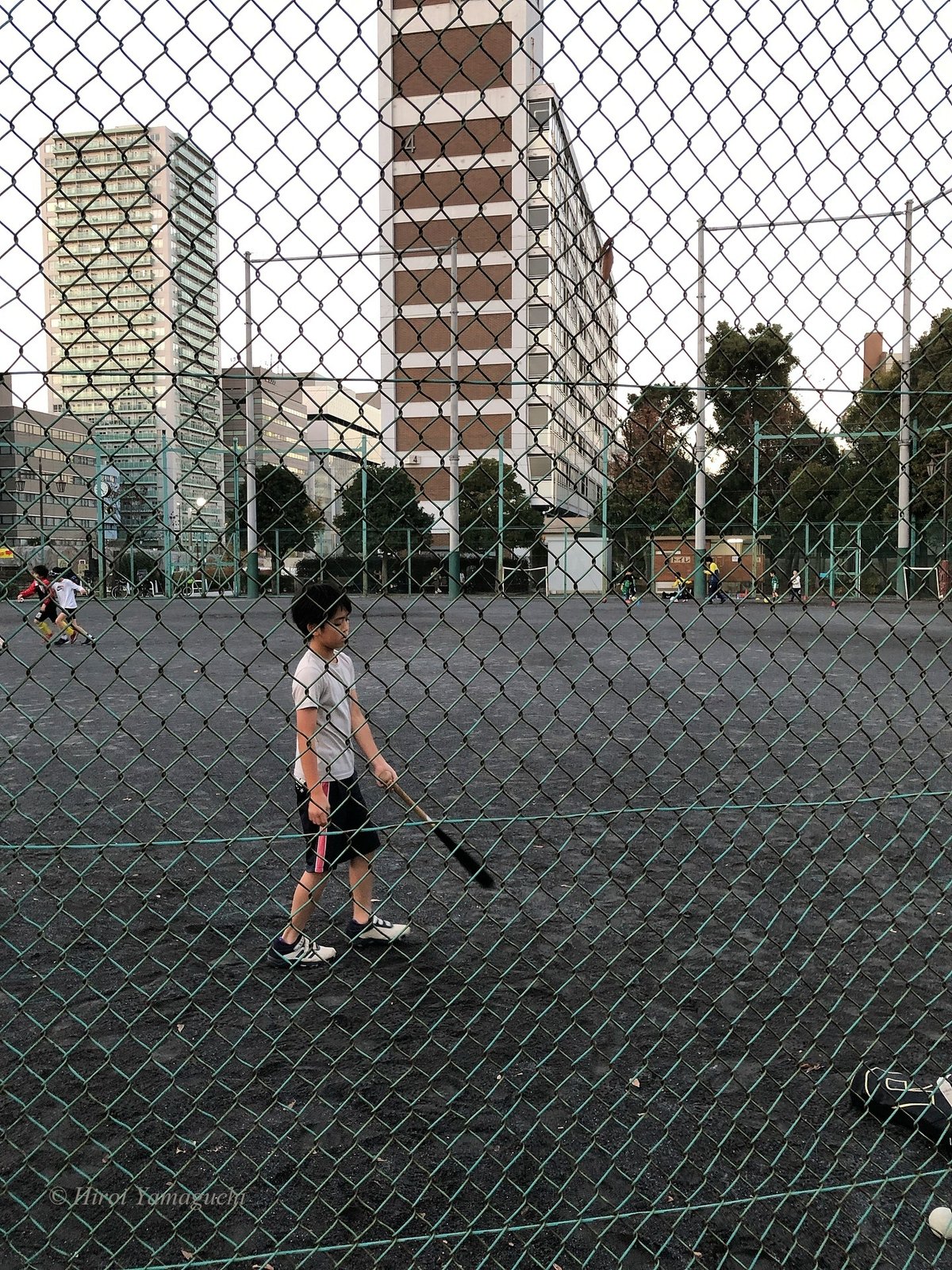 練習場でバットを持つ少年。上手くいかないのか、少し項垂れています。がんばれ！奥では、二人でサッカーをしている少年もいます。