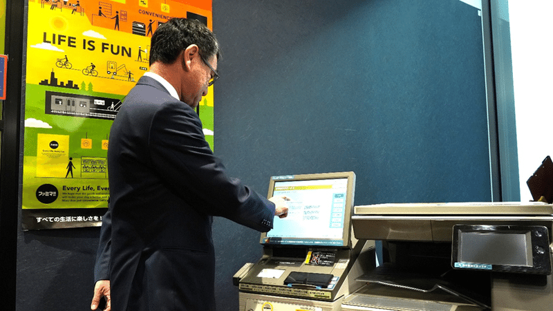河野デジタル大臣が、東京都内のコンビニにおいて、スマホ用電子証明書を活用して、コンビニのキオスク端末（マルチコピー機）より住民票の写し等を交付するサービスを体験している様子