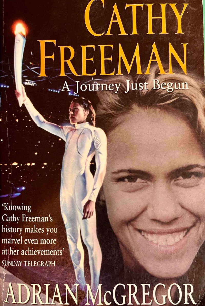 キャシー・フリーマンが全身白いタイツを着て、オリンピックトーチを持って立っている。