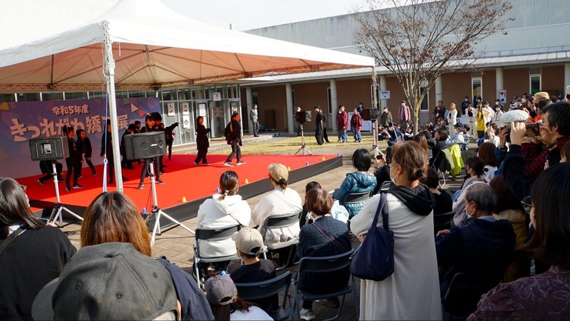 令和5年度きつれがわ矯正展(2023年11月23日開催)で喜連川社会復帰促進センター敷地内の中央に設けられたステージでダンスをする子どもたちと鑑賞する来場者たち