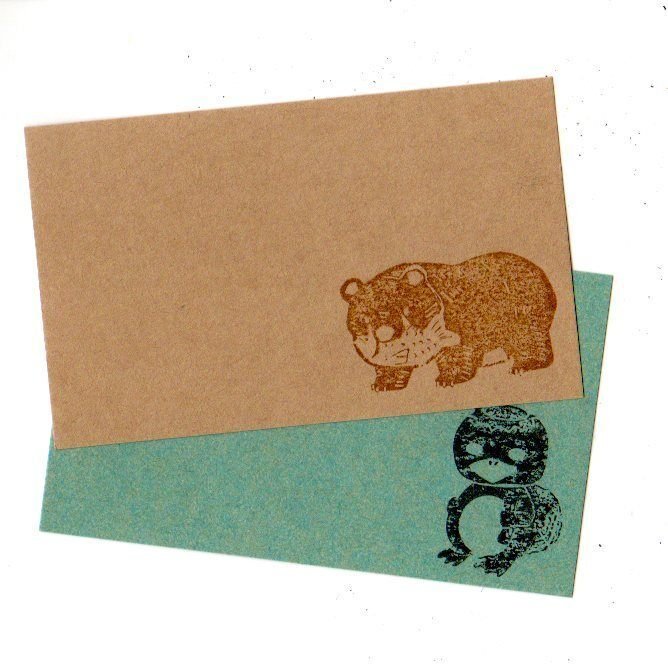 クラフト紙に茶色いインクでスタンプされた木彫りの熊と、緑の紙に黒いインクでスタンプされた河童。