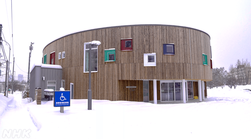 雪の風景のなかに建っている円形の木調の建物の写真。窓がカラフル。