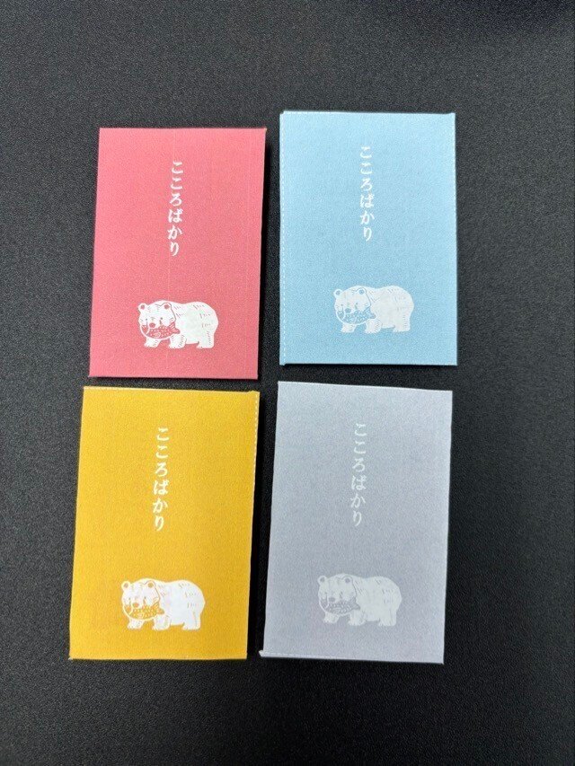 ピンク、水色、黄色、灰色の背景に白抜きで木彫りの熊が配置されたポチ袋4種の画像