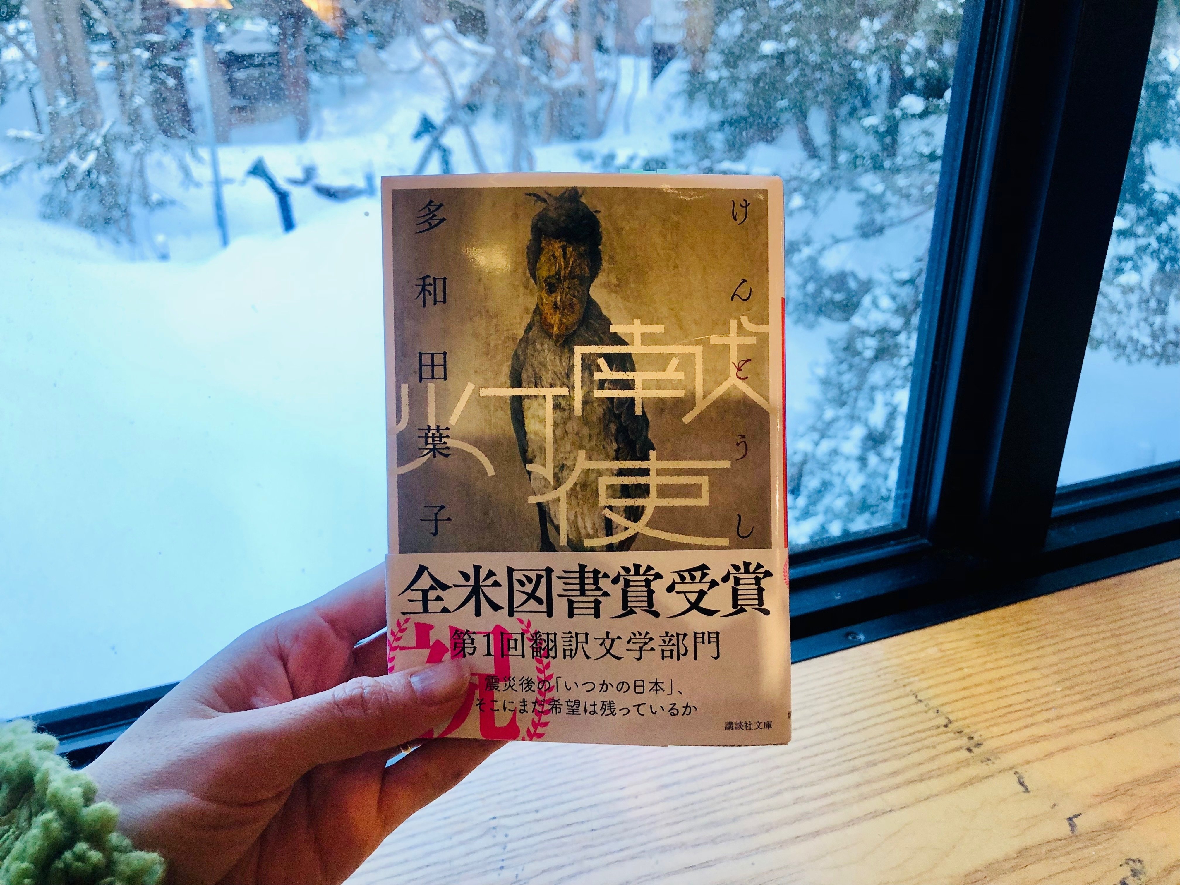 多和田葉子さんの小説『献灯使』。窓際を背に手に持っている。窓の外は一面の雪景色。