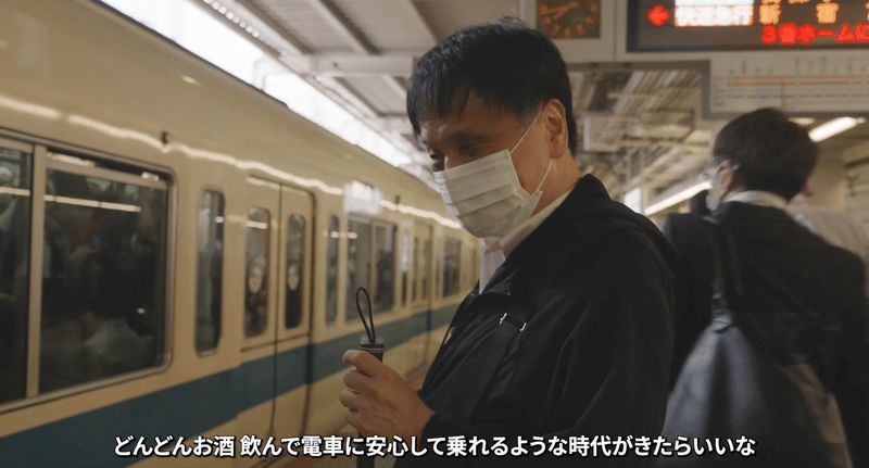 ホームに止まった電車の前に立つ川田さんの画像。「視覚障がい者でもどんどんお酒飲んで電車に安心して乗れるような時代がきたらいいな」と話している。