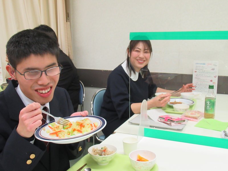 笑顔で食べる卒業生男子と笑顔で見守る指導員