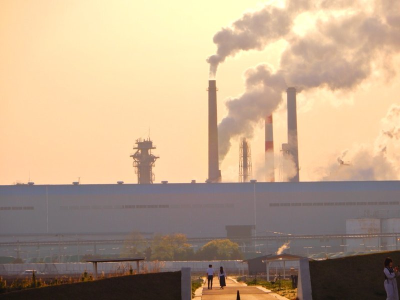 夕日に染まる日本製紙の工場と煙突から登る煙