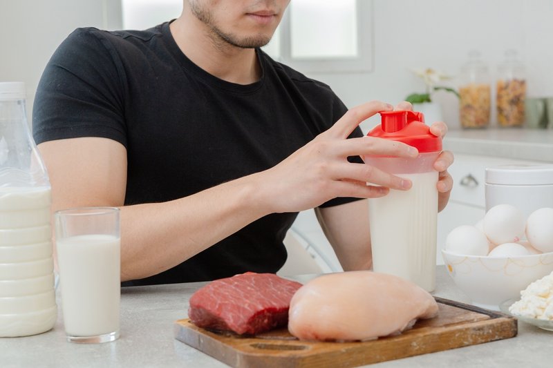 タンパク質を多く含む食品の並んだテーブルと、プロテインを作っている男性の写真