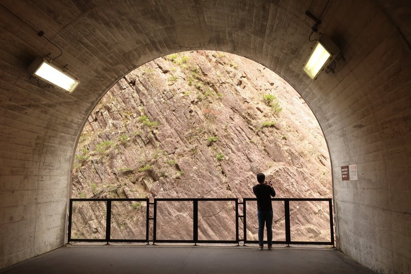 トンネルの途中の空間から渓谷の写真を撮る夫