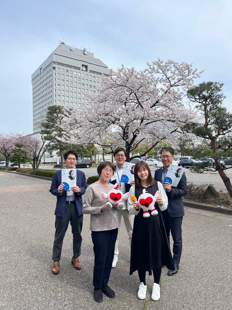 新潟県人事委員会事務局の職員採用担当が新潟県庁を背景に集合している写真