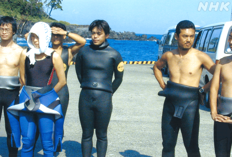 潜水研修時、ウェットスーツを着て並ぶメンバーのなかに立つ望月アナ。その右側に細田アナも。
