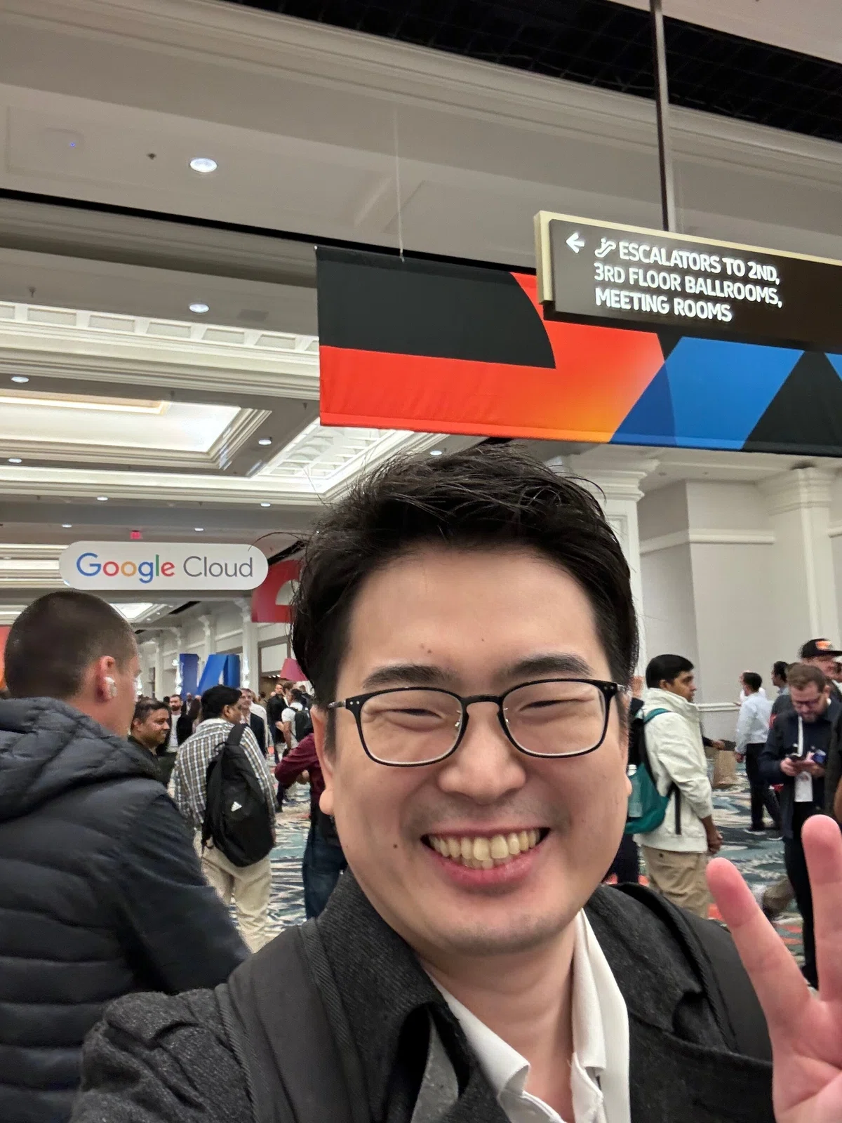 会場の廊下で自撮りする筆者の写真です。後ろに「Google Cloud」と看板が天井から下がっています。多くの人が歩いています。