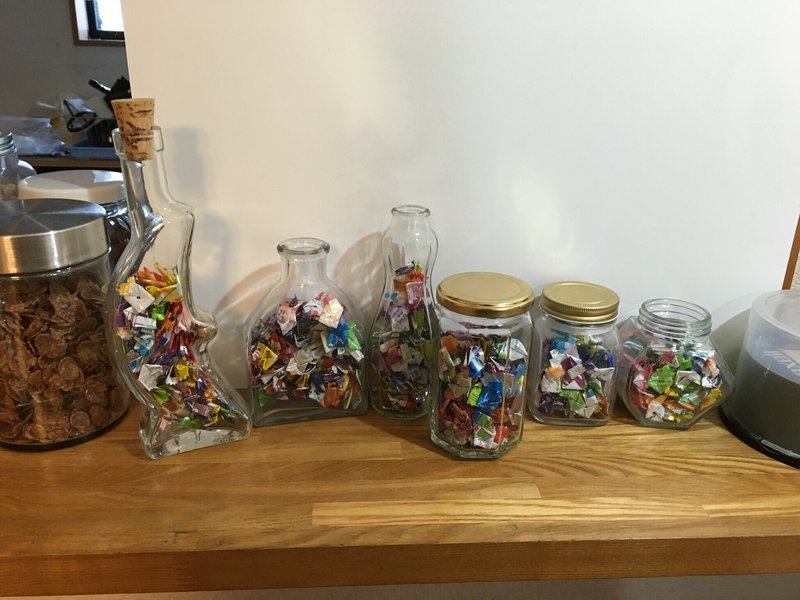 ６つの瓶が並んでおり、中には大量の飴玉の個包装が入っています。小さく畳まれてそれぞれの瓶に入っており、色の統一性はなくカラフルです。