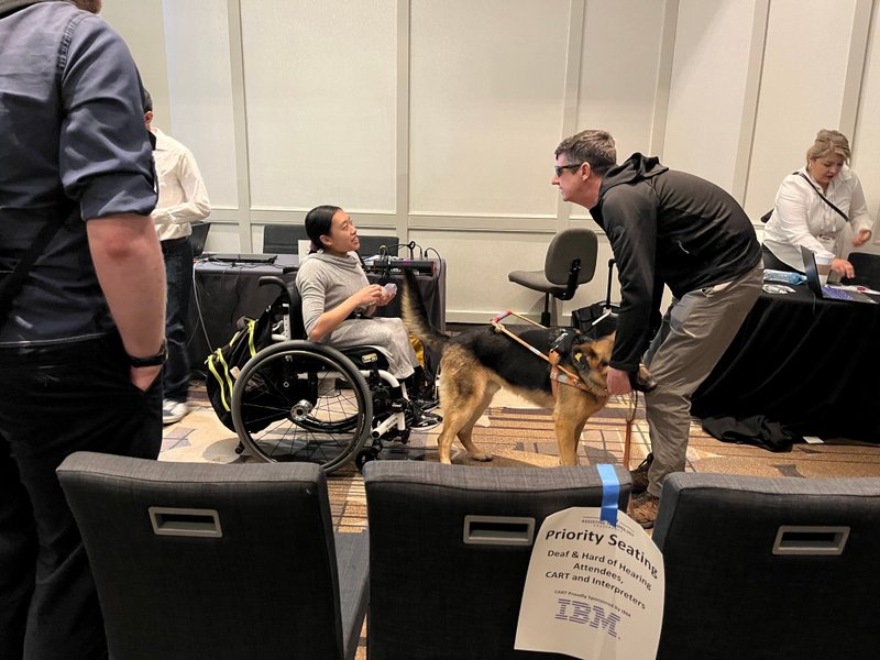 車いすのクリスティンに盲導犬ユーザーが質問をしている。手前のプライオリティシートにはIBMの文字が