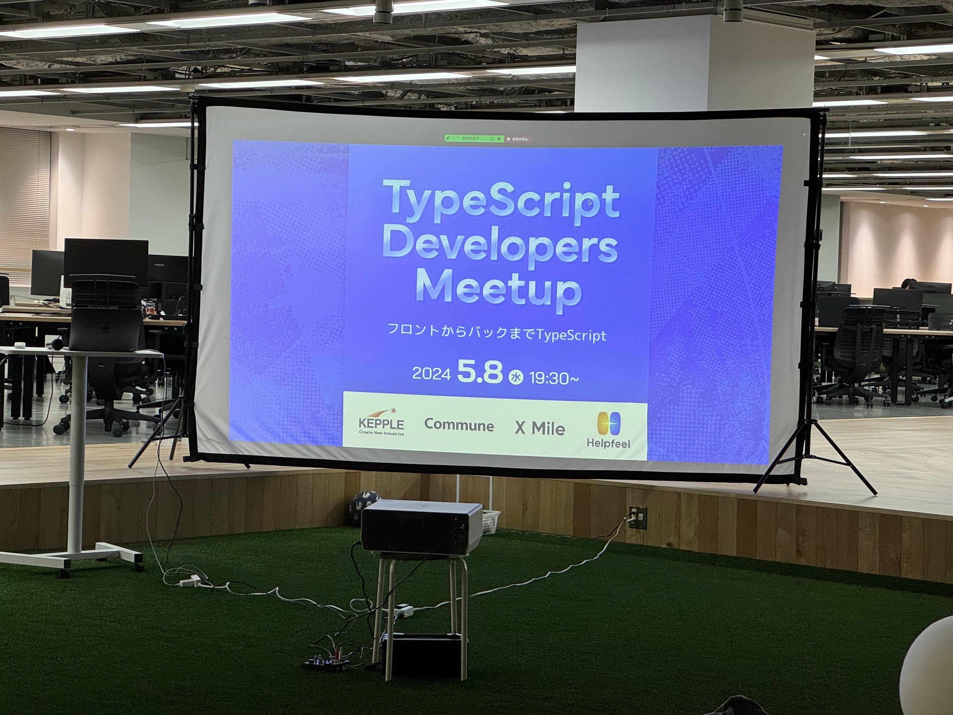 TypeScript Developers Meetupと書かれたスライドが写っている室内の写真です。室内ですが芝生が生えていて、その上にプロジェクターが設置されています。